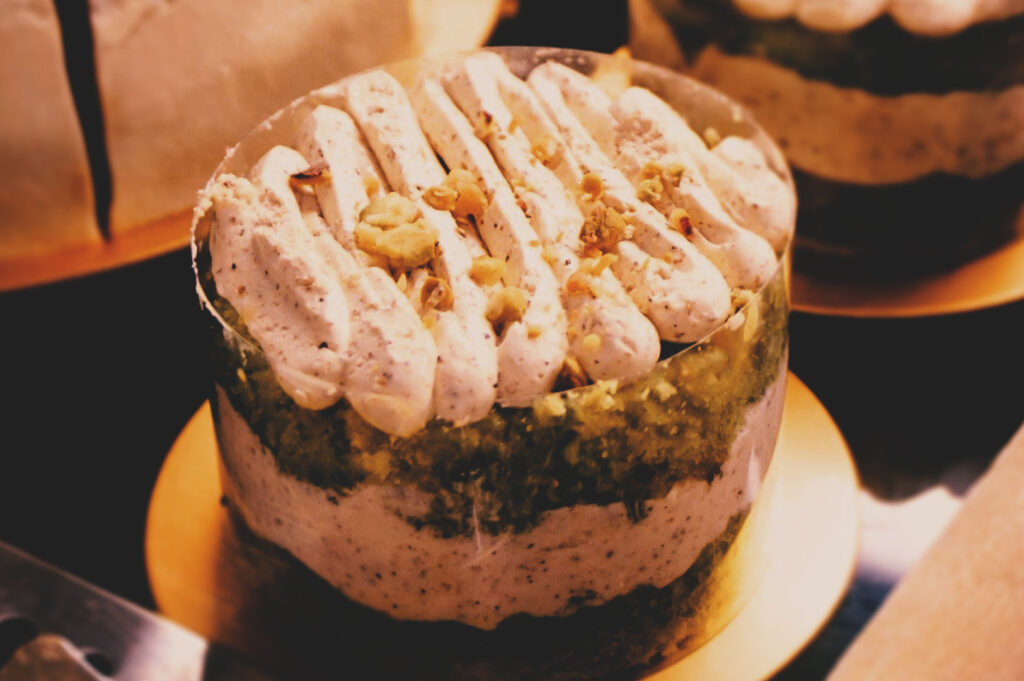 Pistachio cake in clear cylinder with vibrant green sponge, creamy nut filling, piped cream, and chopped pistachio garnish.