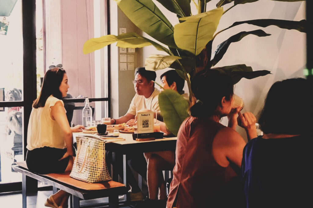 Casual café dining experience with friends and family enjoying food, drinks, and conversation in a bright, modern restaurant interior.