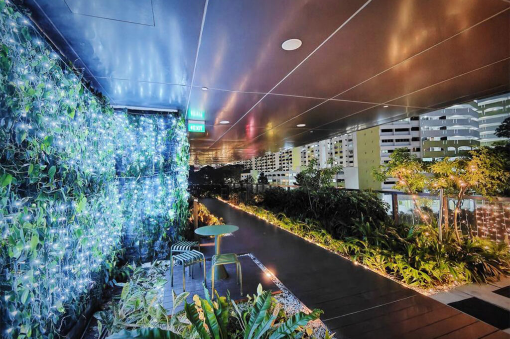 Rooftop garden walkway with greenery and soft evening lights.
