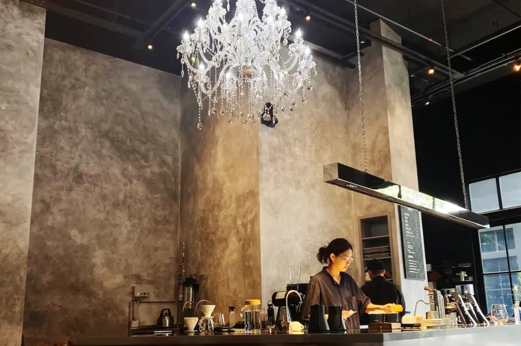 Barista working beneath a crystal chandelier at Alchemist The Mill café in Singapore.