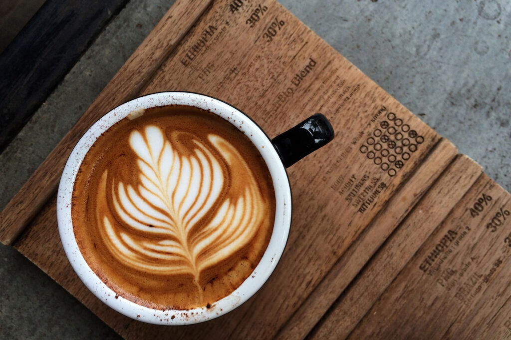 Latte with leaf art on wooden board.