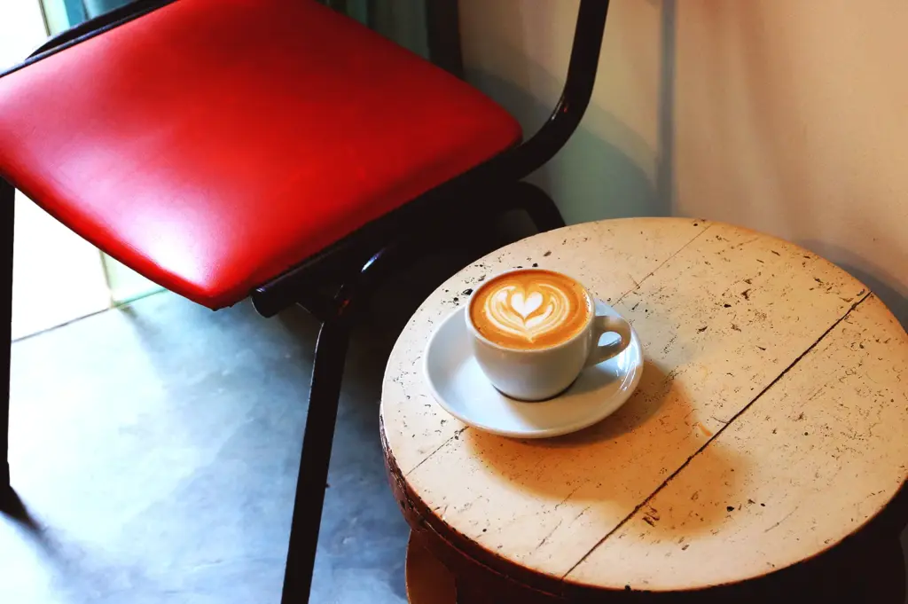 Latte with heart foam on wooden table beside red chair at Nylon Coffee Roasters Singapore showing natural light, shadows, and cafe photography setup