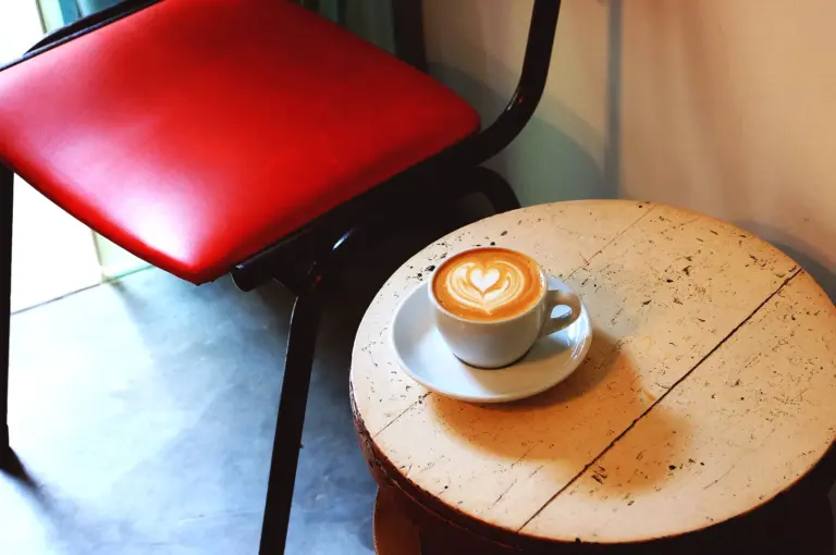 Latte with heart foam on wooden table beside red chair at Nylon Coffee Roasters Singapore showing natural light, shadows, and cafe photography setup