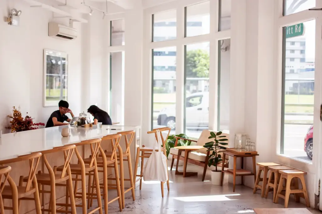 Bright minimalist Singapore cafe interior with window seating and natural light, contrasting popular seating areas versus quiet hidden corners