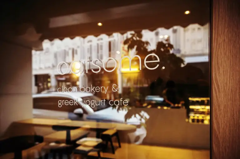 Oatsome Singapore cafe exterior window with reflections of light and greenery showing quiet atmosphere and layered glass perspective