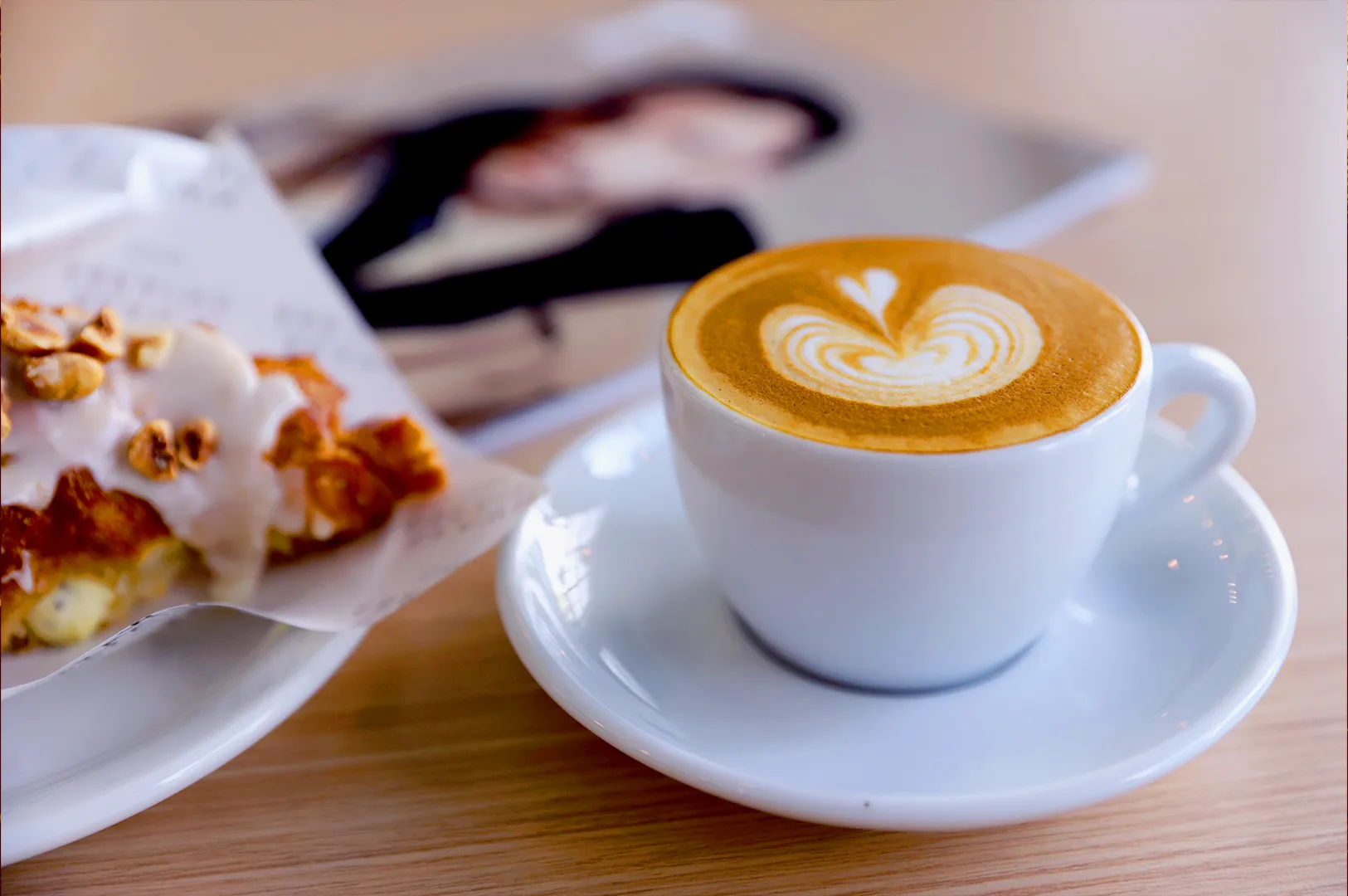 Latte with heart art and pastry at Fahrenheit Coffee Singapore on wooden table showcasing minimalist cafe food and coffee presentation