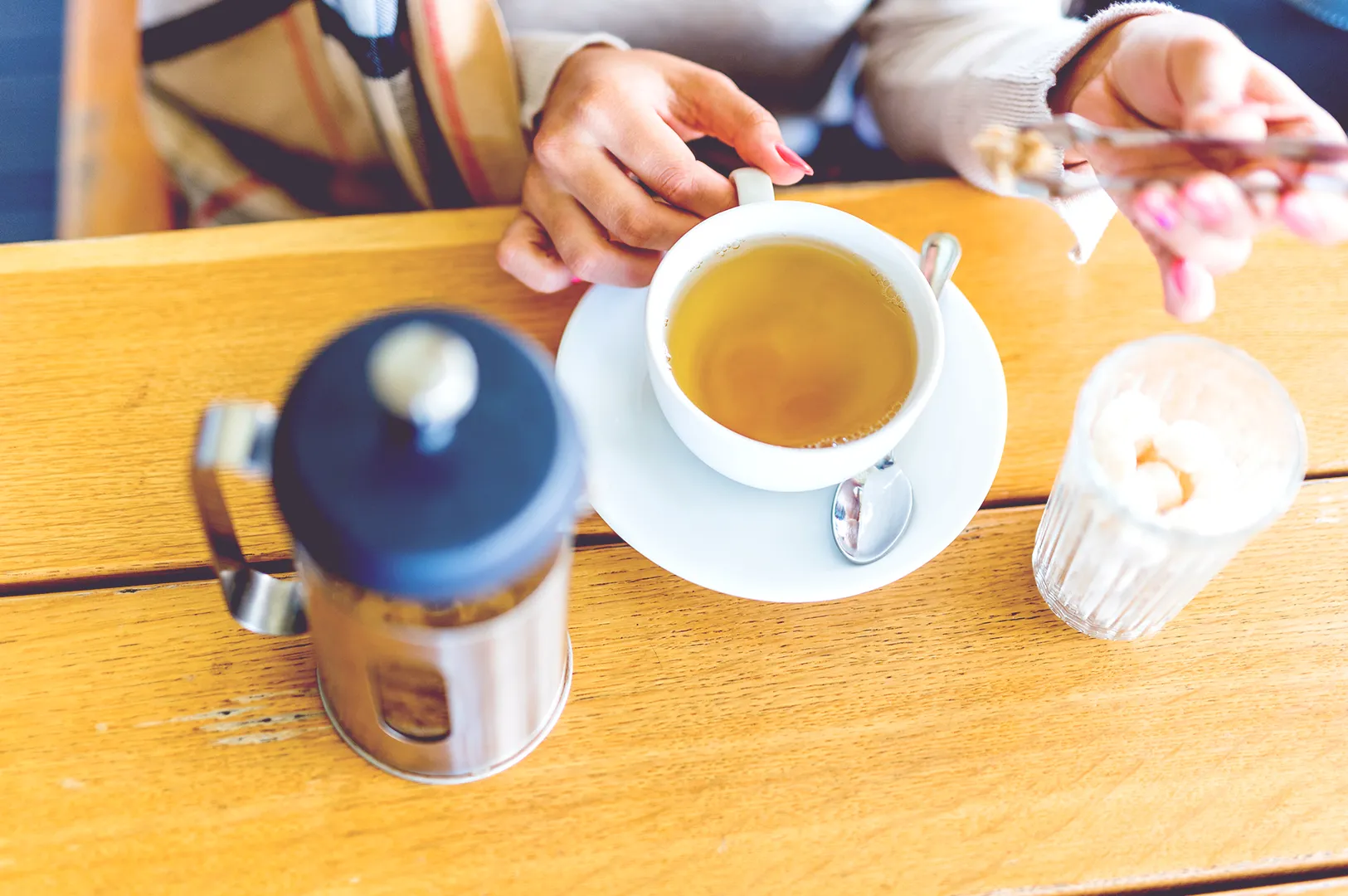 Pouring tea into cup with teapot and sugar on wooden table