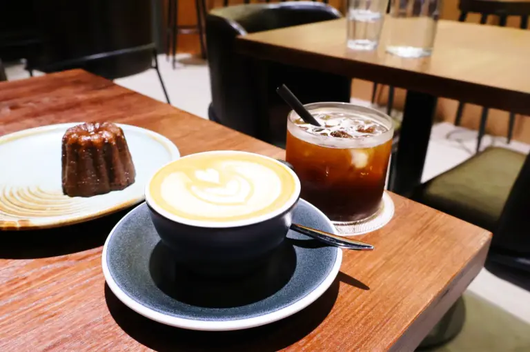 Latte art coffee, iced drink, and canelé on wooden table at Chapter One by Fables Specialty Coffee Singapore showing minimal presentation and cafe ritual