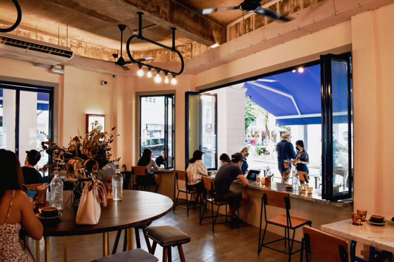 Warm Singapore cafe interior with open window seating, marble counter tables, and natural daylight pouring into a busy specialty coffee space