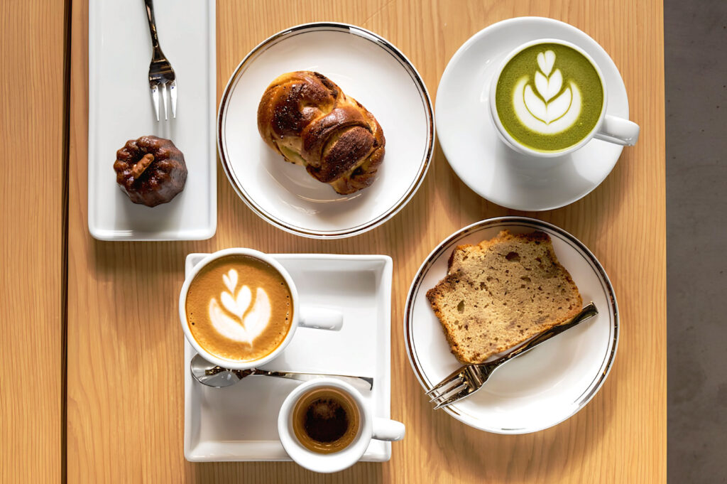 Cozy overhead cafe breakfast spread with matcha latte art, espresso, pastries, and wooden table ambiance in Singapore cafe