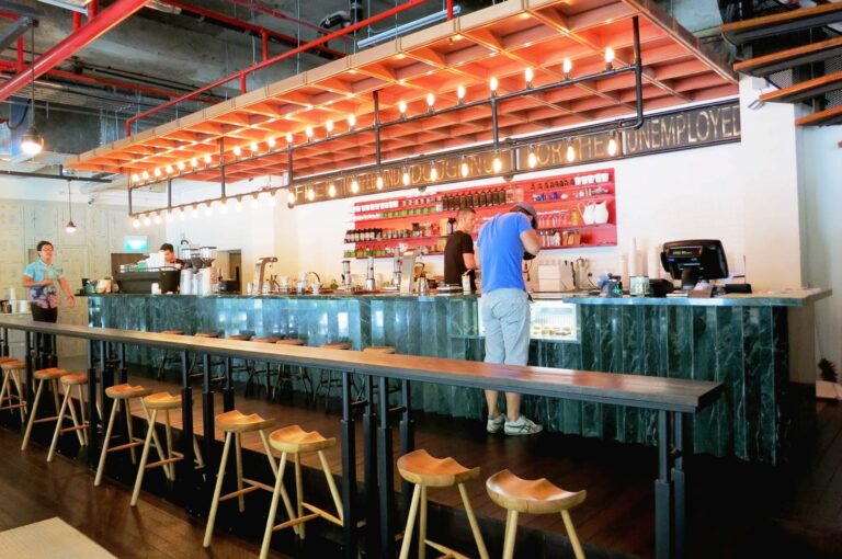 Common Man Coffee Roasters Singapore interior with long bar seating, open kitchen, and warm industrial lighting creating a lively cafe atmosphere
