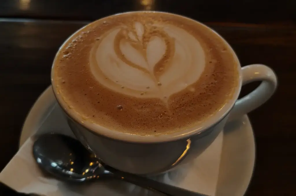 Latte with heart-shaped foam art on saucer.
