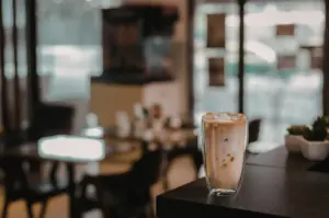 A tall glass of iced coffee with cream and ice sits on a dark counter in a cafe.