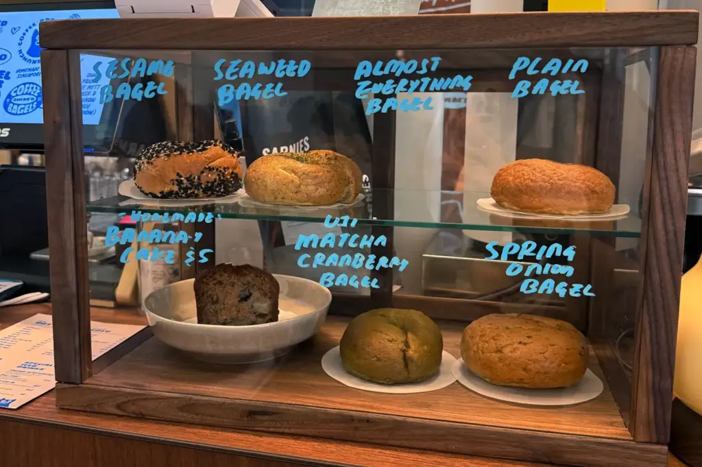 Bagels in a glass display case with handwritten labels.