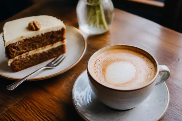 Coffee cup with collapsed milk foam beside layered cake slice on wooden cafe table